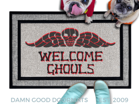 a french bulldog and a fawn pug dog in hoodies sitting on a door mat with the text "WELCOME GHOULS" and a spooky Beetlejuice tombstone on it.